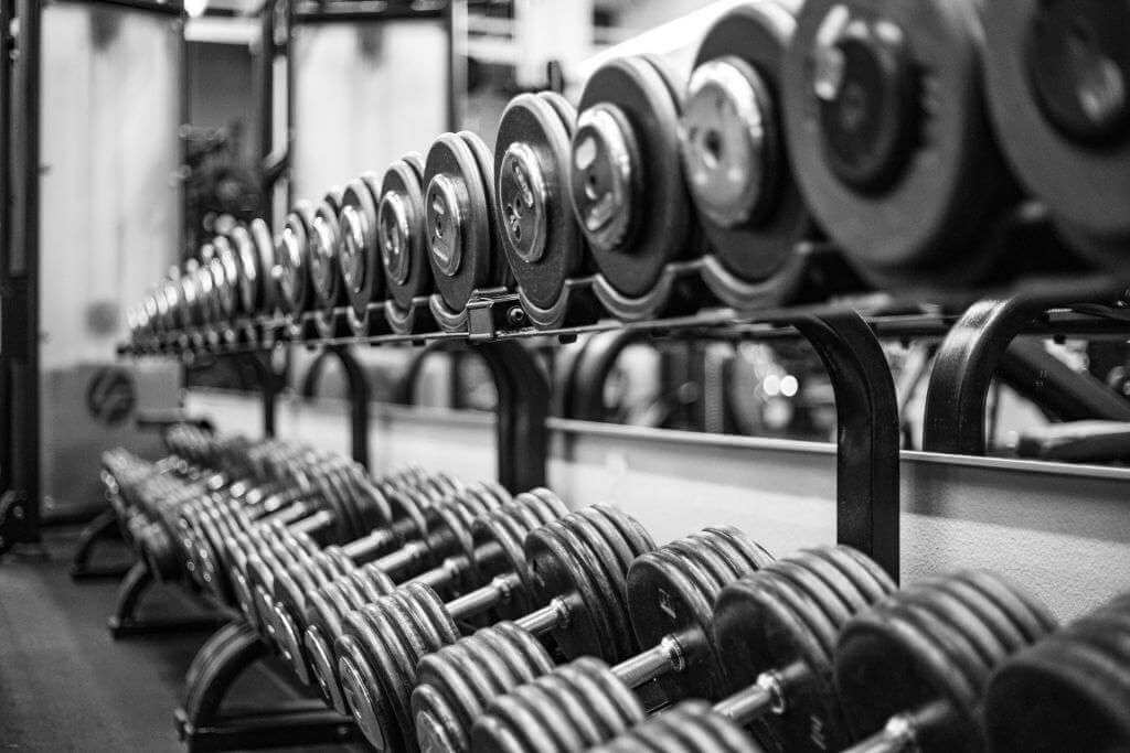 A black-and-white image of a gym's weight rack filled with rows of dumbbells, reminiscent of TouchDesigner visuals. Dumbbells are neatly arranged on two levels of the rack.