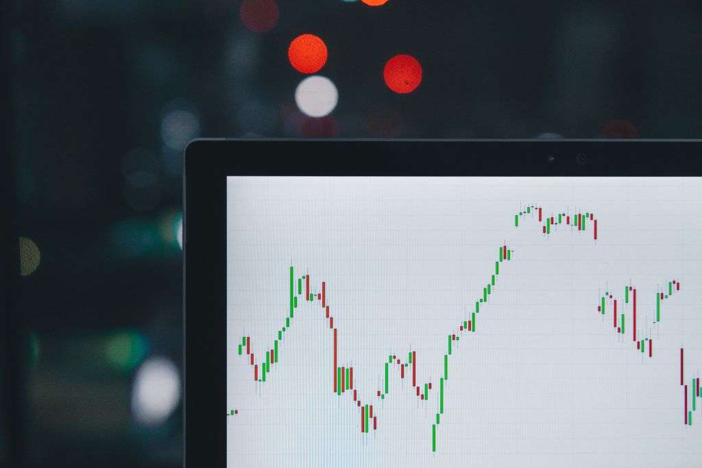 A computer screen displays a fluctuating stock market chart with candlestick patterns, created using TouchDesigner, set against a blurred background with out-of-focus lights.