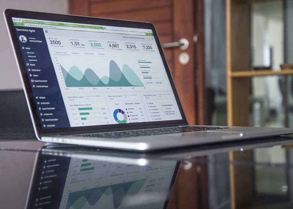 A laptop on a reflective surface displays a TouchDesigner dashboard with various graphs, charts, and statistics for website analytics.